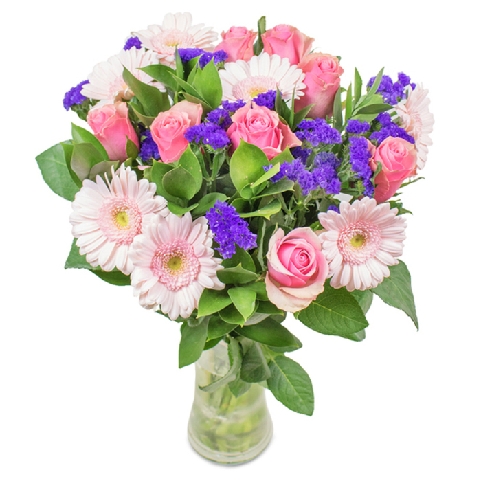 This radiant bouquet, skilfully arranged in Elmers End and presented in a clear glass vase against a pure white backdrop, highlights the artistry and freshness at the core of every local flower delivery. At its heart are seven to nine medium-pink roses, their petals elegantly swirling in classic spiral forms, some tightly cupped, others just opening to reveal their intricate beauty. Complementing the roses are five to seven pale pink gerbera daisies, each with generous, rounded heads and a halo of slender, radiating petals; their centres fade to near white, adding a subtle contrast and airiness to the display. Scattered through the bouquet, clusters of vibrant purple statice or limonium create a striking interplay of colour and texture, their vivid hue adding depth reminiscent of Elmers End's springtime bluebells. Glossy green foliage weaves between blossoms, providing a lush, abundant base that feels both natural and invigorating-much like the neighbourhood's green spaces. Visible stems within the water-filled vase highlight the arrangement's just-picked freshness, suggesting the care of a passionate Elmers End florist. This bouquet is an inspired choice for birthdays, anniversaries, or simply to bring a burst of celebration and affection into a home or office across Elmers End, radiating feelings of joy and thoughtful artistry.